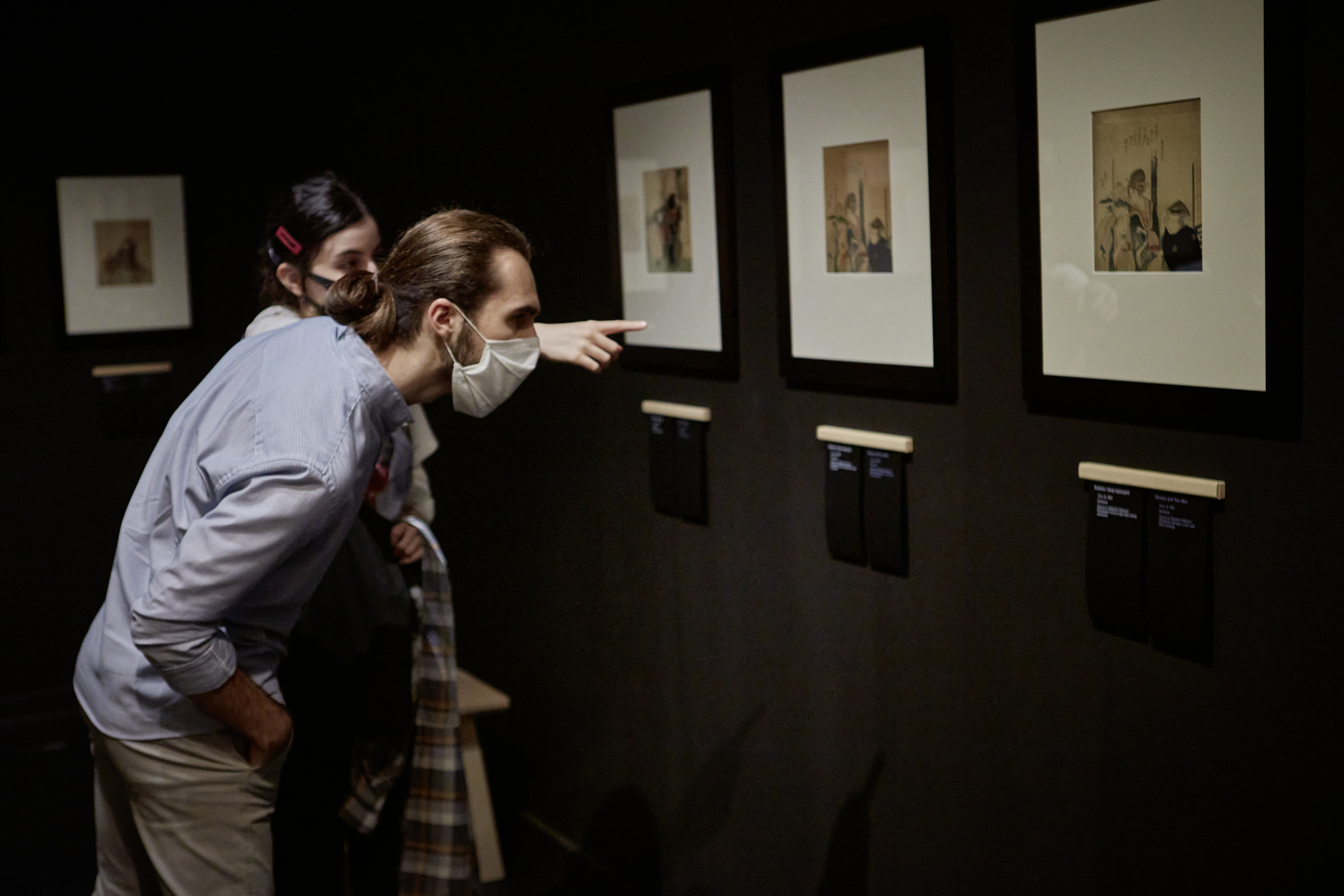Dwójka uczestników projektu “Spektrum” zwiedza wystawę Hokusaia. Młoda kobieta wskazuje palcem na drzeworyt przedstawiający kobietę i dwóch mężczyzn, a stojący przed nią chłopak schyla się, by przeczytać podpis pod innym drzeworytem.