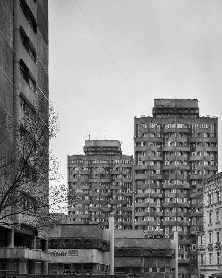 Eksponowane na wystawie pt. “Przekroje” zdjęcie dwóch betonowych wieżowców z zespołu mieszkalno-usługowego przy placu Grunwaldzkim we Wrocławiu. Elewację budynków wyróżniają okrągłe osłony przy oknach. Na dachach budynków są niewielkie nadbudówki. 