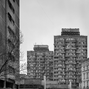 Eksponowane na wystawie pt. “Przekroje” zdjęcie dwóch betonowych wieżowców z zespołu mieszkalno-usługowego przy placu Grunwaldzkim we Wrocławiu. Elewację budynków wyróżniają okrągłe osłony przy oknach. Na dachach budynków są niewielkie nadbudówki. 