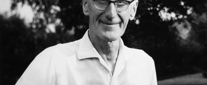 Czarno-biała fotografia przedstawiająca Józefa Czapskiego. Artysta na zdjęciu jest już stary, jest częściowo łysy i ma siwe włosy. Nosi czarne okulary. Ma na sobie jasną, gładką koszulę. Za nim widać pokryte liśćmi gałęzie drzew.