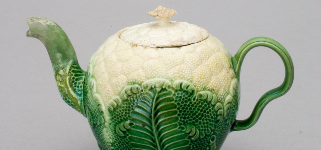 Zbliżenie ceramicznego imbrzyka z teksturowanym wzorem liści, zielono‑kremową szkliwą, widocznym dzióbkiem po lewej, pokrywką z małym uchwytem na górze i zakrzywioną rączką po prawej na jasnoszarym tle.