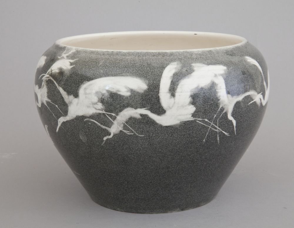 Zaokrąglony ceramiczny pojemnik o szarym, drobnoziarnistym szkliwie z pasmem białych sylwetek ptaków w locie wokół górnej części, kremowym wnętrzem i jednolitym szarym tłem.
