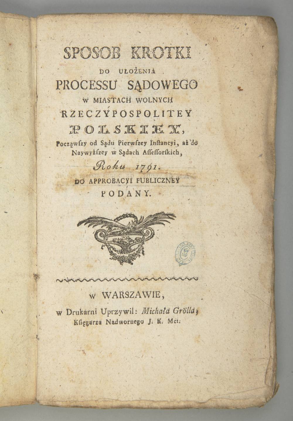 Strona tytułowa starej, pożółkłej książki w języku polskim z dużym drukowanym tytułem u góry, kilkoma blokami tekstu w środku, ozdobnym rytowanym emblematem z motywem roślinnym poniżej, niewyraźną okrągłą pieczęcią, plamami i postrzępionymi brzegami papieru.