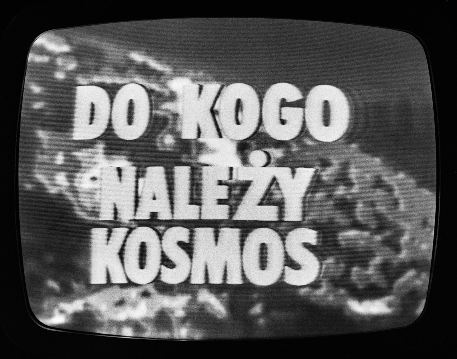 Czarno-białe zdjęcie ekranu telewizora z zaokrąglonymi rogami, na którym na trzech liniach dużymi białymi blokowymi literami wyświetlony napis DO KOGO NALEŻY KOSMOS na rozmytym, chmurowym tle.