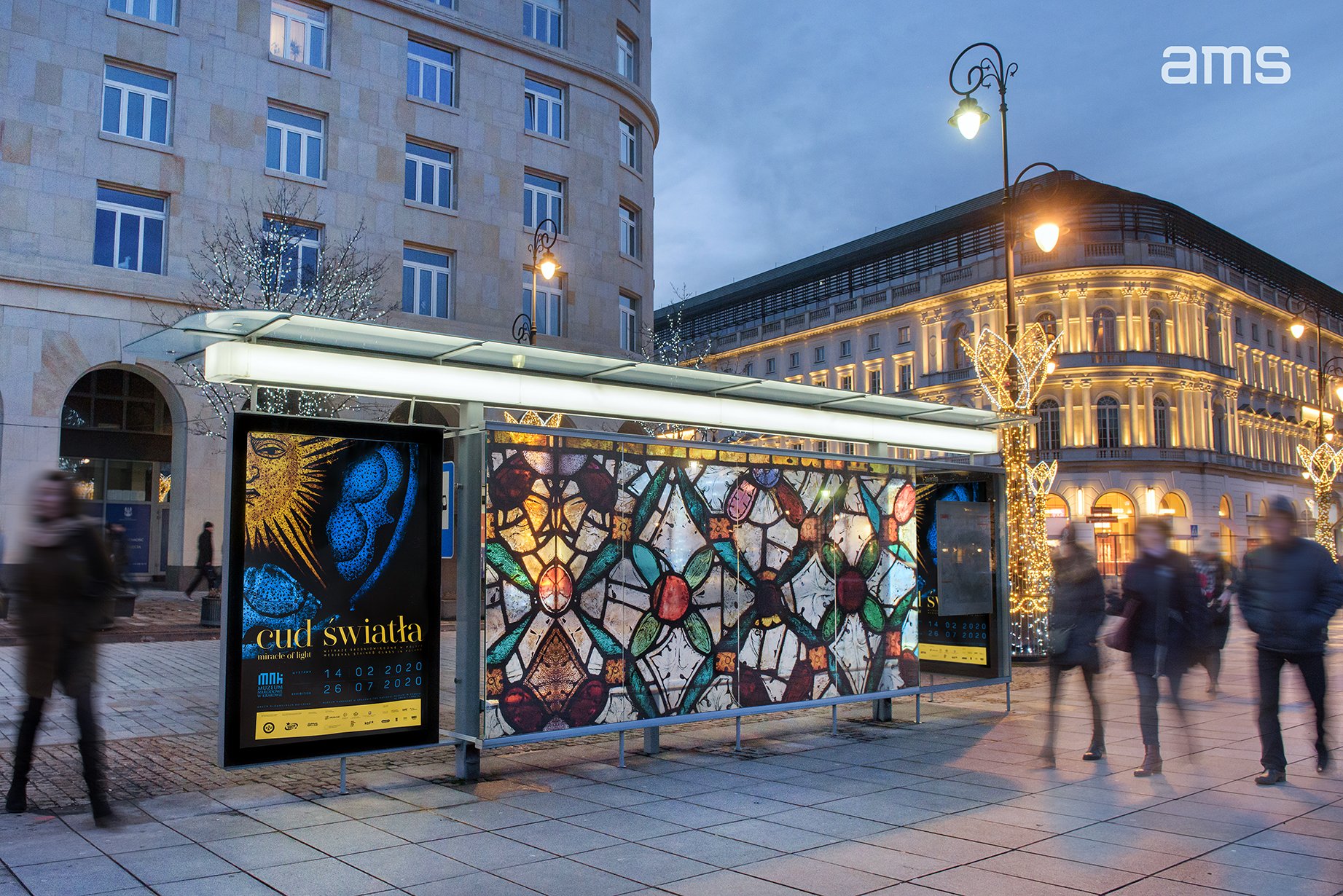 Wieczorna scena miejskiego przystanku z oszkloną wiatą reklamową, na której widoczna jest duża tablica z motywem kolorowego witrażu i plakatem cud światła; w tle podświetlone kamienice, ozdobne latarnie z dekoracjami świetlnymi, choinkowe światełka, rozmyci przechodnie na kamiennym chodniku i logo ams w prawym górnym rogu.