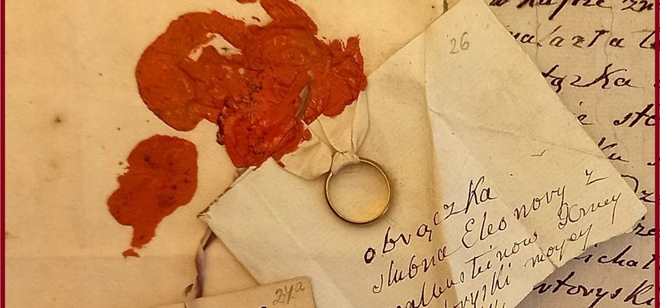 Zbliżenie na pożółkłe, złożone listy i koperty z odręcznym pismem; do jednej koperty przywiązany wąską wstążką złoty pierścionek, obok kilka rozmazanych czerwonych plam laku pieczętniczego.