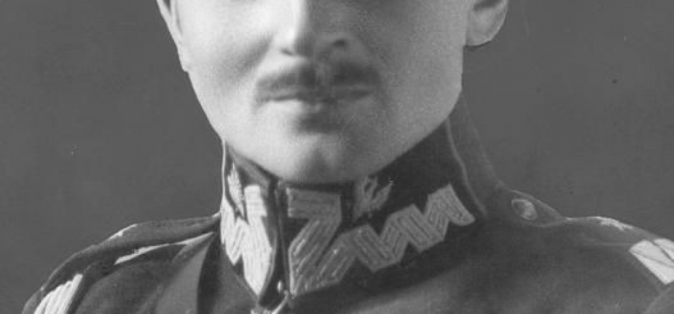 Czarno-białe zdjęcie fragmentu twarzy osoby z wąsem, ukazujące dolną część twarzy od nosa do ramion w wojskowym mundurze z wysokim, ozdobnym kołnierzem z haftowanym wzorem.