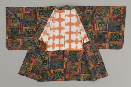 Rozłożone na płasko kimono o szerokich rękawach, z zewnętrzną tkaniną w wielobarwny geometryczny wzór z kwadratami i zygzakami oraz białym podszyciem z powtarzającym się pomarańczowym motywem przypominającym chmury, na jednolitym jasnym tle.