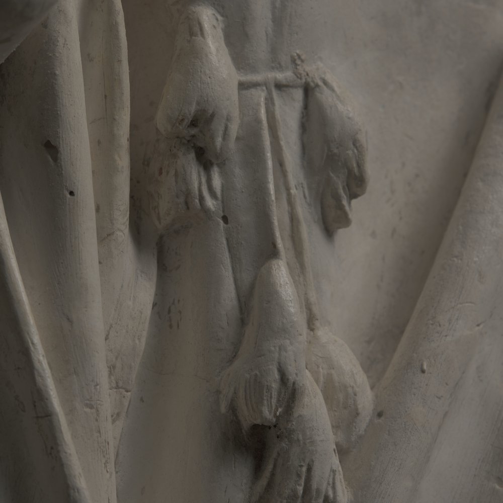 Zbliżenie na biało‑szary relief rzeźbiarski z cienkimi łodygami i kilkoma wiszącymi, dzwonkowatymi kwiatami oraz chropowatą, miejscami popękaną powierzchnią materiału.