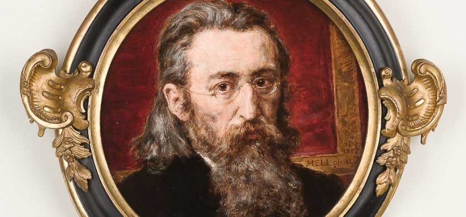 Owalny portret malarski przedstawiający mężczyznę z długimi włosami, gęstą siwą brodą i wąsami oraz drobnymi okularami, na ciemnoczerwonym tle, oprawiony w czarno‑złotą ozdobną ramę z rzeźbionymi złotymi ornamentami.