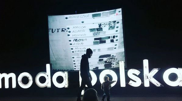 Na ciemnym tle sylwetki dorosłej osoby i dziecka trzymających się za ręce przechodzą przed dużym podświetlonym napisem "modapolska", a za nimi widać jasny ekran z listą imion i kilkoma kolorowymi paskami.