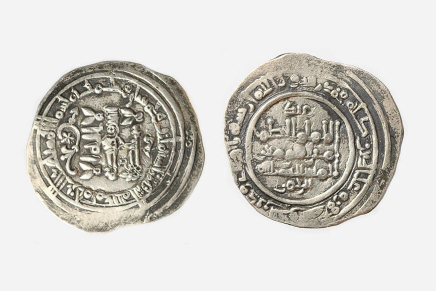 Dwie nieregularne srebrne monety ułożone obok siebie na jasnym tle, każda z gęstym arabskim pismem, okrągłymi ozdobnymi obwódkami i widocznymi śladami zużycia.