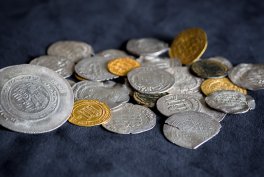 Rozsypane srebrne i złote monety różnych rozmiarów i kształtów leżą na ciemnym materiale, niektóre nachodzą na siebie.