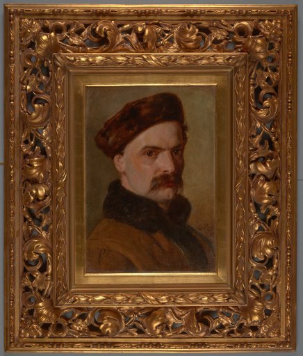 Portret olejny przedstawiający mężczyznę w ujęciu trzy czwarte, w futrzanej czapce i z futrzanym kołnierzem, na stonowanym brązowo‑zielonym tle, oprawiony w bogato rzeźbioną złotą ramę z dekoracyjnymi motywami roślinnymi.