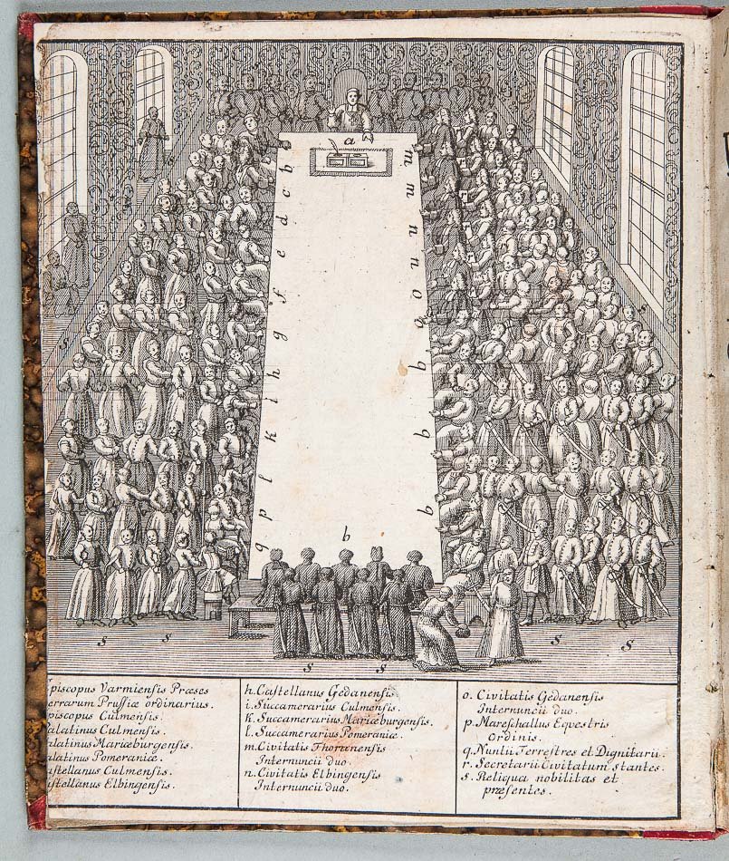 Czarno-biała rycina na stronie książki przedstawiająca dużą salę z szeroką, pustą prostokątną przestrzenią pośrodku oznaczoną literami, gęstymi rzędami stojących i siedzących postaci w długich szatach po obu stronach, na górze podwyższone biurko z jedną osobą, w pierwszym planie mała grupa postaci zwrócona ku środkowi, po bokach wysokie wieloprzęsłowe okna i wzorzyste ściany oraz u dołu trzy kolumny z legendą zawierającą łaciński tekst.