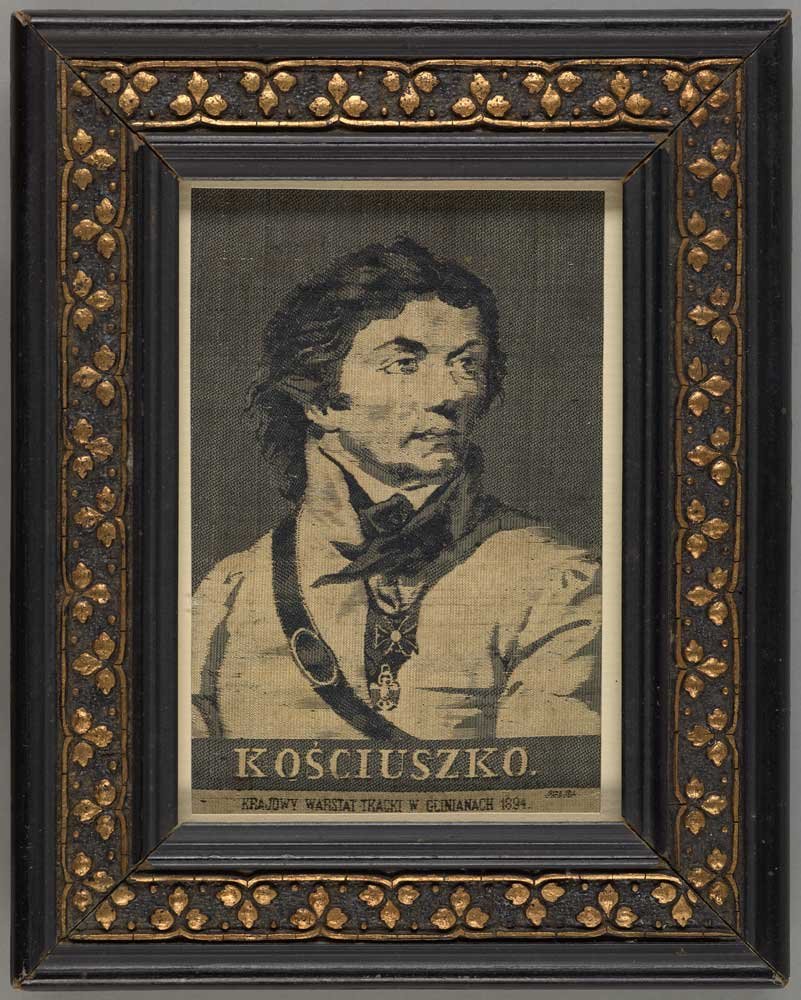 Portretowy rysunek w tonacji czarno‑beżowej przedstawiający popiersie mężczyzny w stroju historycznym zwróconego trzy czwarte w prawo, oprawiony w ozdobną czarną ramę ze złotymi motywami liściastymi, z wyraźnym napisem "KOŚCIUSZKO" pod wizerunkiem i drobnym drukiem poniżej.