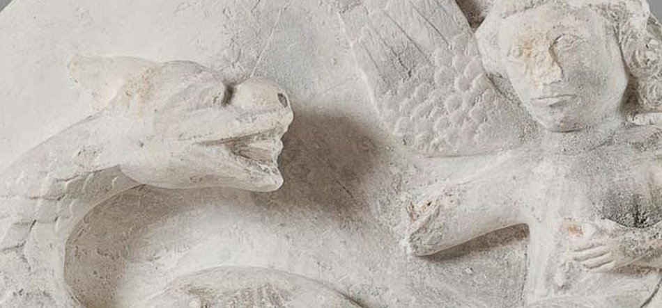 Jasnobeżowy kamienny relief z lewej przedstawiający dużego węża z otwartym pyskiem i widocznymi łuskami oraz z prawej schematyczną postać człowieka z krótkimi włosami i częściowo uniesioną ręką, o powierzchni mocno startego i popękanego kamienia.