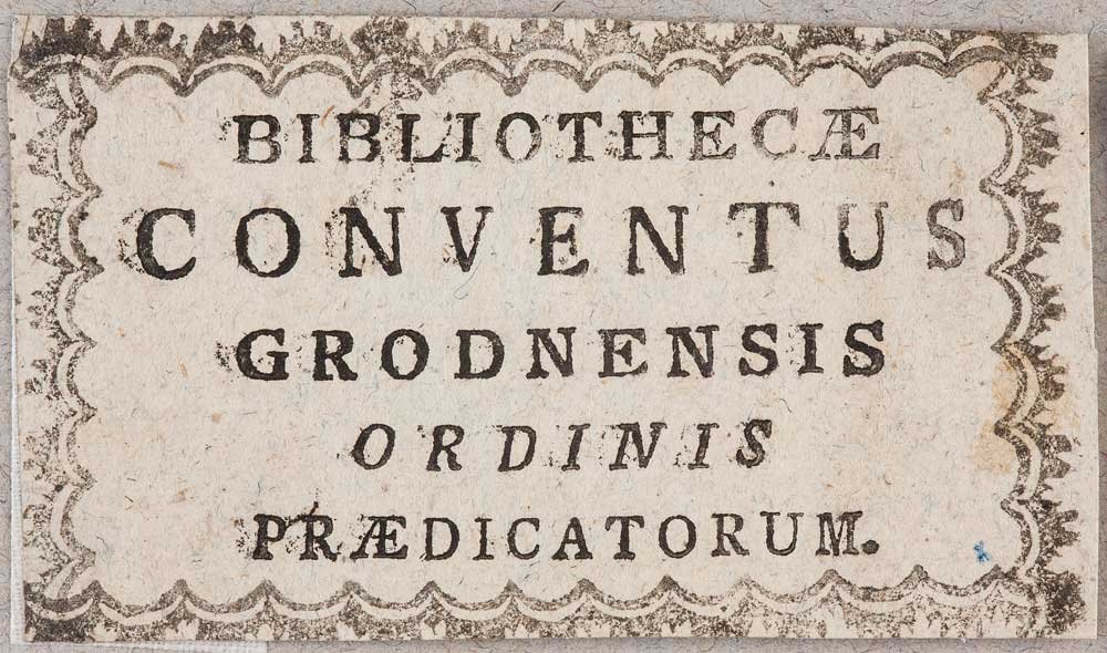 Stara papierowa etykieta z ozdobnym ząbkowanym brzegiem i czarnym drukowanym tekstem łacińskim ułożonym w pięciu wierszach BIBLIOTHECÆ CONVENTUS GRODNENSIS ORDINIS PRÆDICATORUM na lekko poplamionym, postarzałym tle.