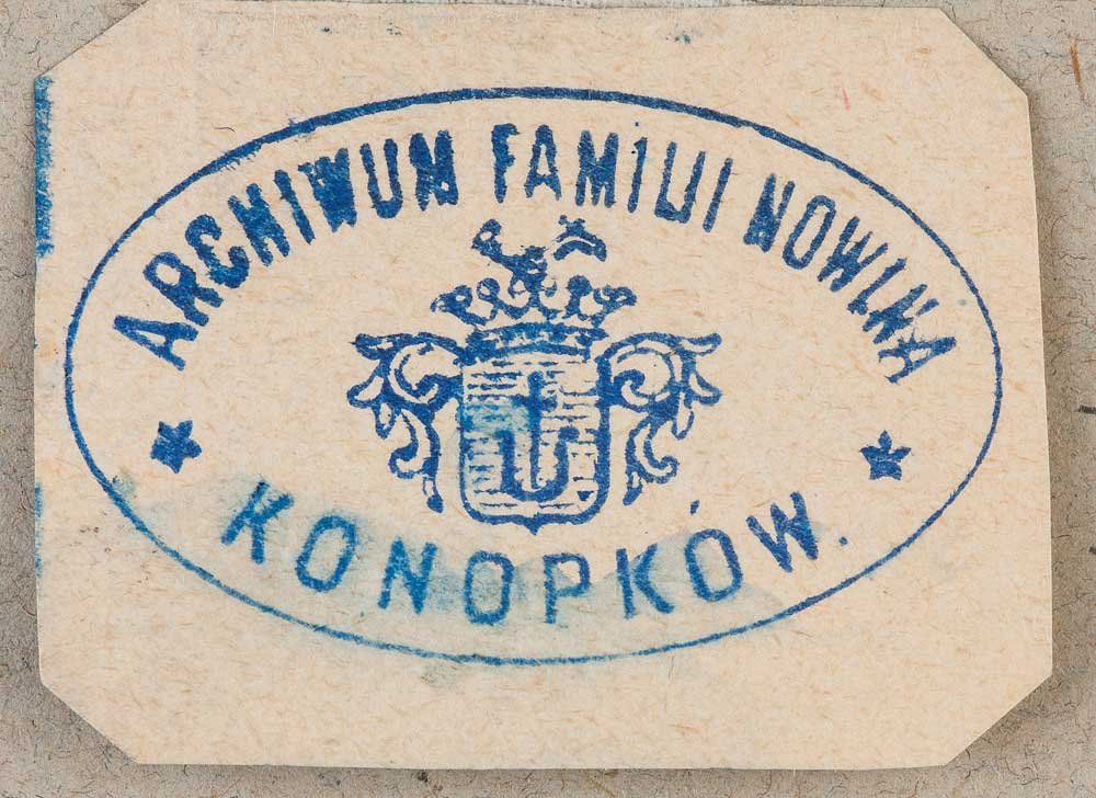 Niebieska owalna pieczęć odbita na beżowym kartoniku z obciętymi narożnikami; w środku herb z koroną i tarczą, u góry łukowy napis ARCHIWUM FAMILII NOWIKA, u dołu napis KONOPKOW. i po bokach dwie gwiazdki.