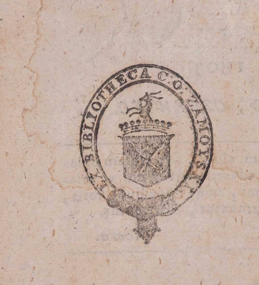 Czarny, owalny ex libris odciśnięty na pożółkłym, poplamionym papierze; w obwodzie częściowo czytelny napis BIBLIOTHECA, wewnątrz tarcza herbu z ukośnym krzyżem, koroną nad tarczą i stylizowaną sylwetką zwierzęcia na górze oraz ozdobną zawieszką u dołu owalu.