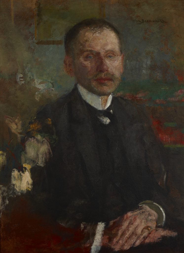 Portret olejny mężczyzny w trzech czwartych, siedzącego w ciemnym garniturze z białym kołnierzem i ciemną muszką, z krótkimi ciemnymi włosami i wąsami, z rękami spoczywającymi na stole po prawej stronie i trzymającymi okrągły metalowy przedmiot, na rozmytym, teksturowanym tle w odcieniach zieleni, czerwieni i brązu z kremowymi pociągnięciami pędzla.