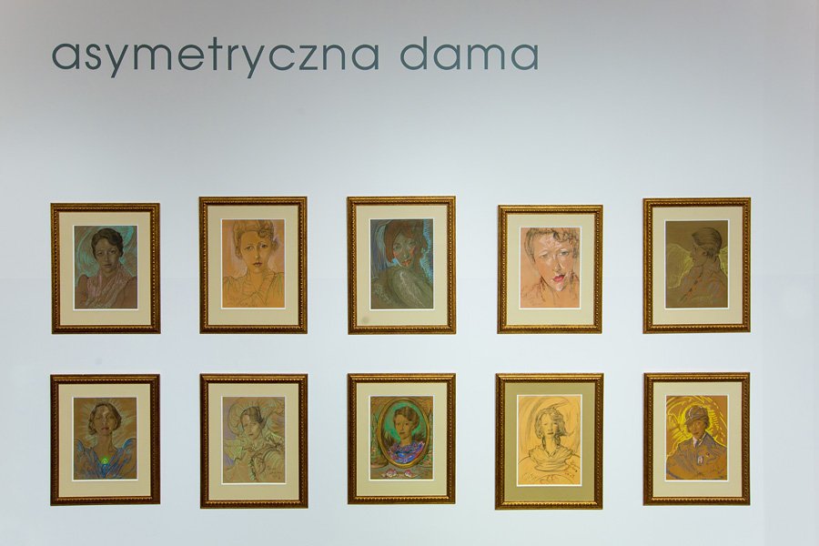 Dziesięć złotych, oprawionych portretów rysowanych pastelami ułożonych w dwóch równych rzędach na białej ścianie pod dużym napisem asymetryczna dama.