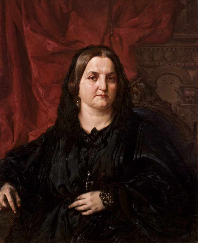 Portret siedzącej dojrzałej kobiety w czarnym żałobnym stroju i koronkowym welonie, z dłońmi spoczywającymi na kolanach, dużą czarną broszą i wiszącym różańcem z krzyżykiem, na tle czerwonej zasłony i ozdobnego rzeźbionego oparcia krzesła.