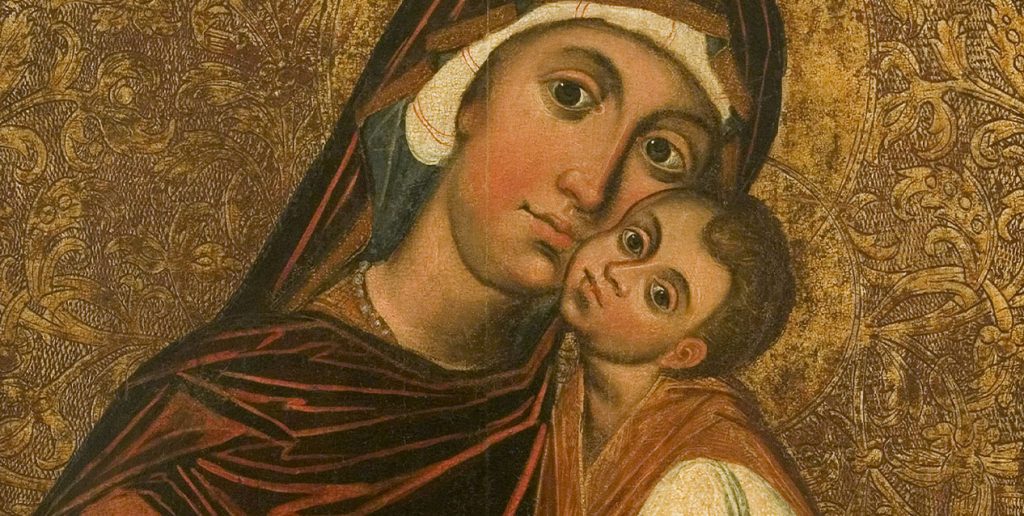 Zbliżenie na ikoniczny obraz religijnny przedstawiający kobietę w ciemnoczerwonym płaszczu i białym nakryciu głowy trzymającą dziecko przytulone policzkiem do jej twarzy, obie postacie z dużymi oczami i aureolami na tle złocistego, bogato ornamentowanego wzoru.