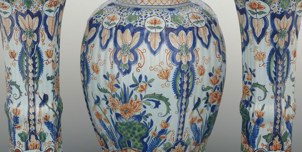 Zbliżenie trzech ceramicznych wazonów — centralnego szerokiego, zaokrąglonego w kształcie amfory między dwiema wyższymi, wąskimi formami — wszystkie pokryte misternym, powtarzalnym malowanym wzorem z stylizowanych kwiatów, liści, palmet i drobnych ptaków w odcieniach kobaltu, zieleni i pomarańczu na jasnym tle.