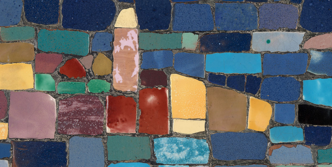 Mozaika ceramicznych, nieregularnych prostokątnych i kwadratowych płytek wypełniająca kadr, w różnych odcieniach niebieskiego, turkusu, zieleni, czerwieni, żółci, różu i brązu, z ciemnymi fugami oraz błyszczącymi, spękanymi i nakrapianymi szkliwami.